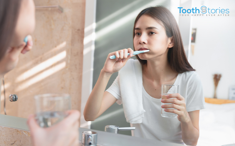 Girl brushing her teeth with holding glass of water